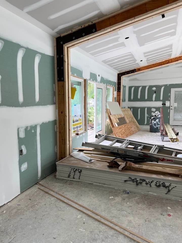 Interior construction in progress, drywall installed on walls and ceiling, doorway to outside view.