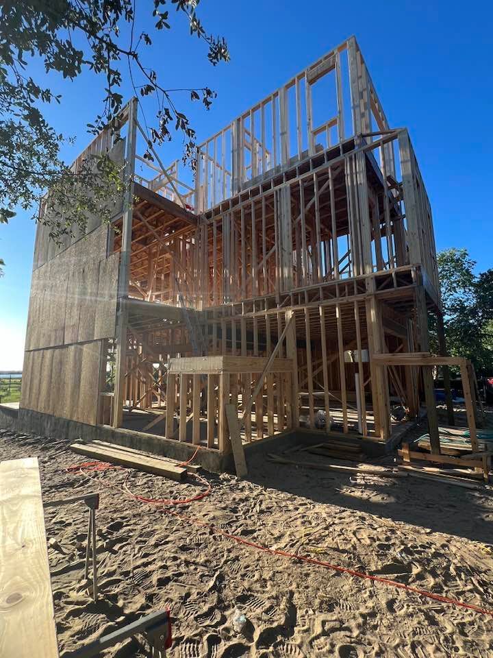 A large wooden house is being built on a sandy beach.