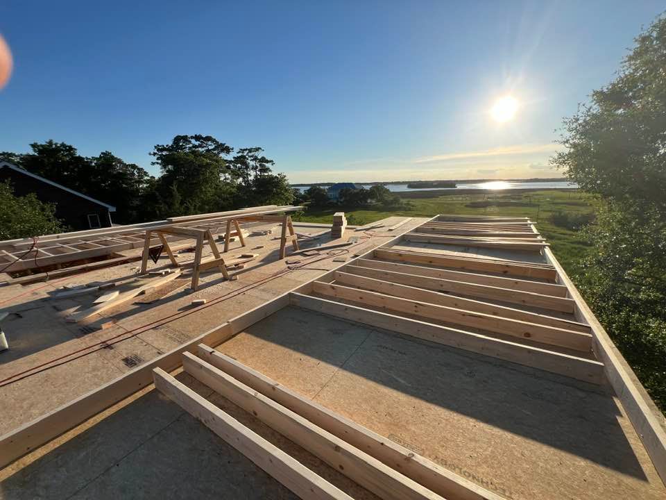 Construction of a wooden floor, sunny outdoors, with a clear view of the water and sky.