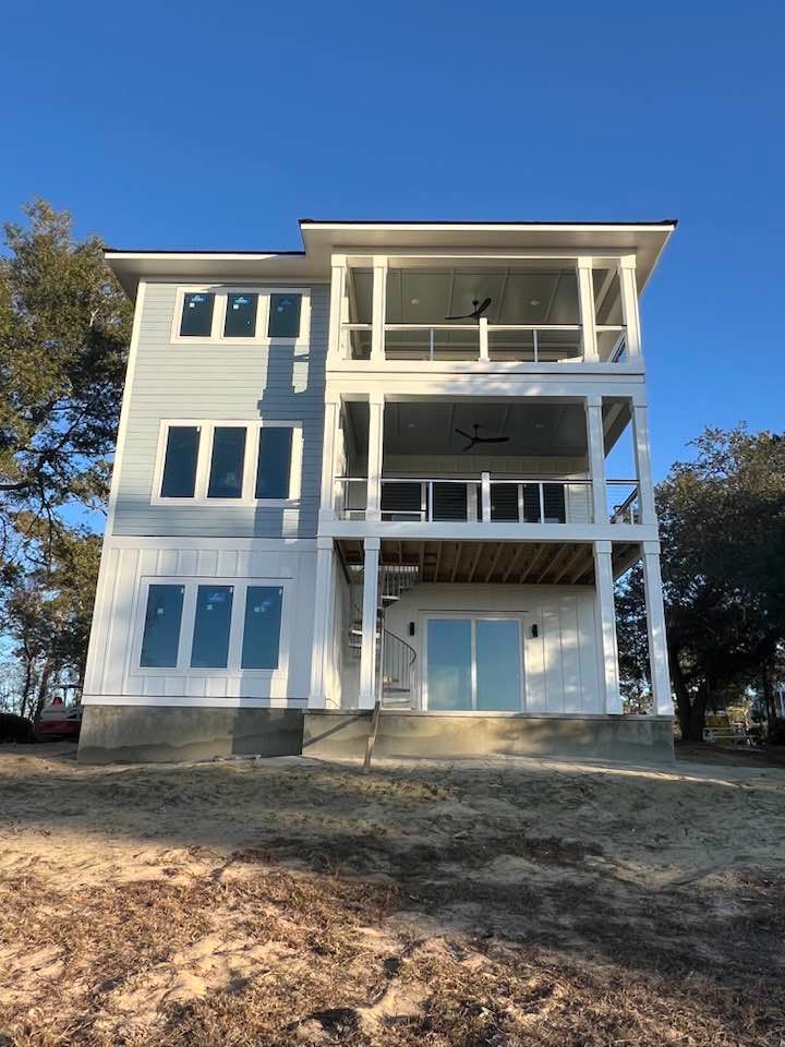 Three-story light blue and white house with multiple decks, next to trees, on a sunny day.