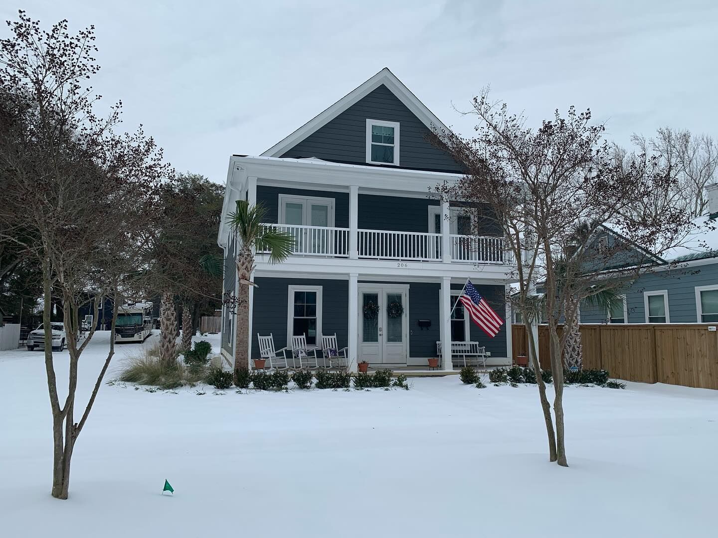 Two-story blue house with white trim in a snowy yard; American flag on the porch.