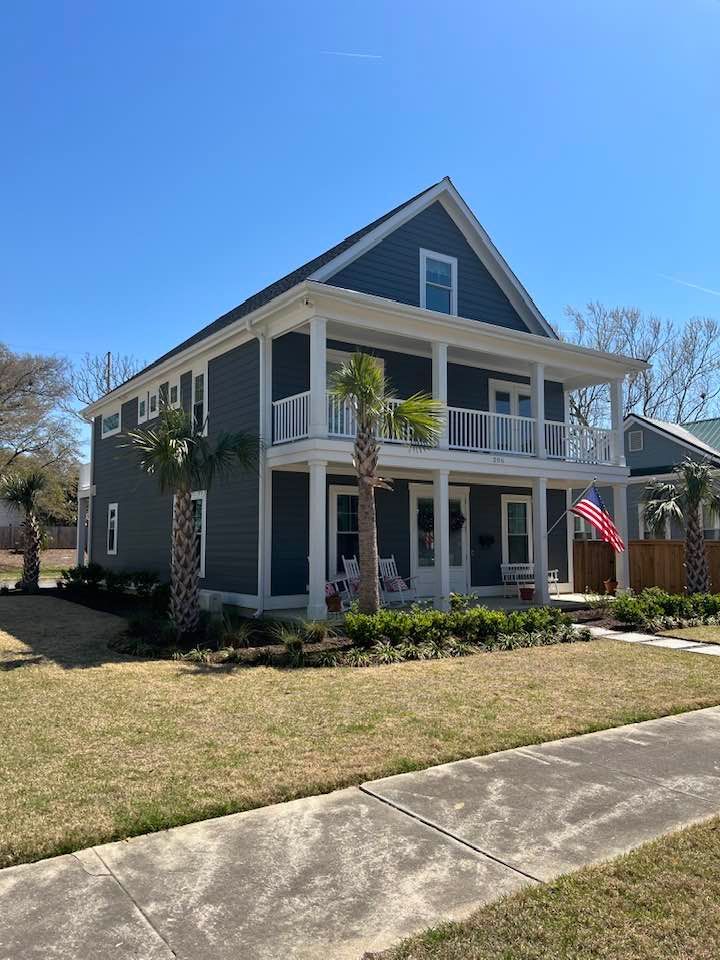 Two-story blue house with white trim and balconies, palm trees, and an American flag.