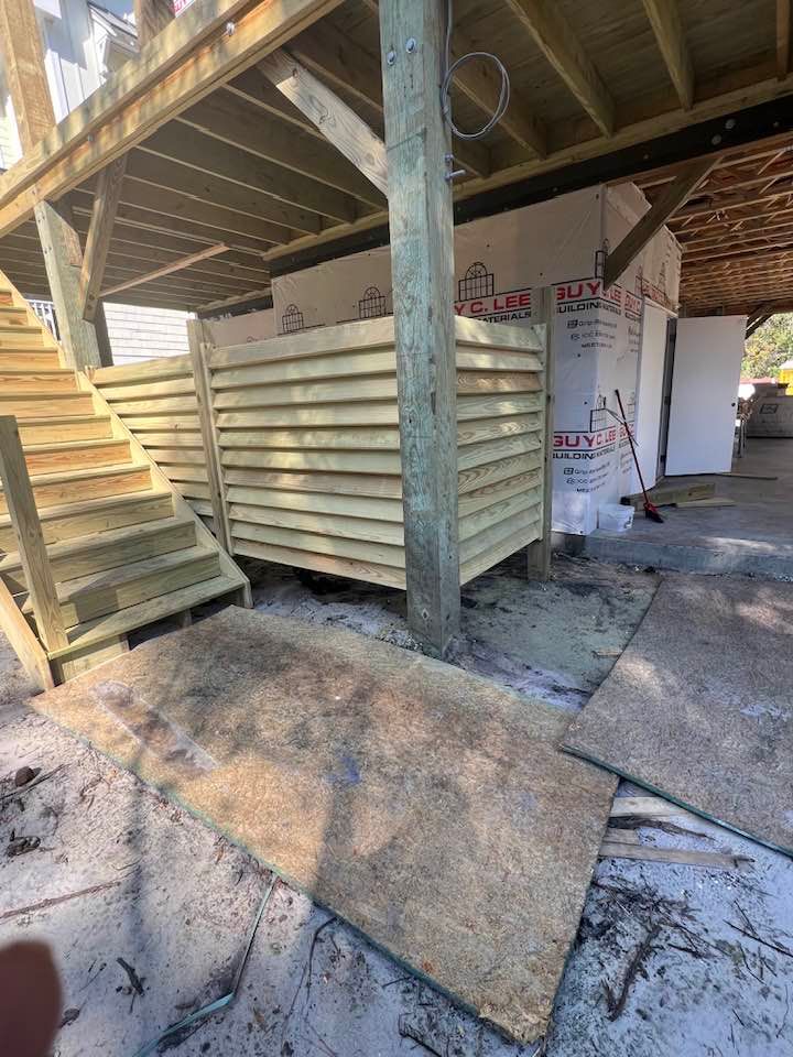Wooden outdoor shower under a deck, stairs to the left.