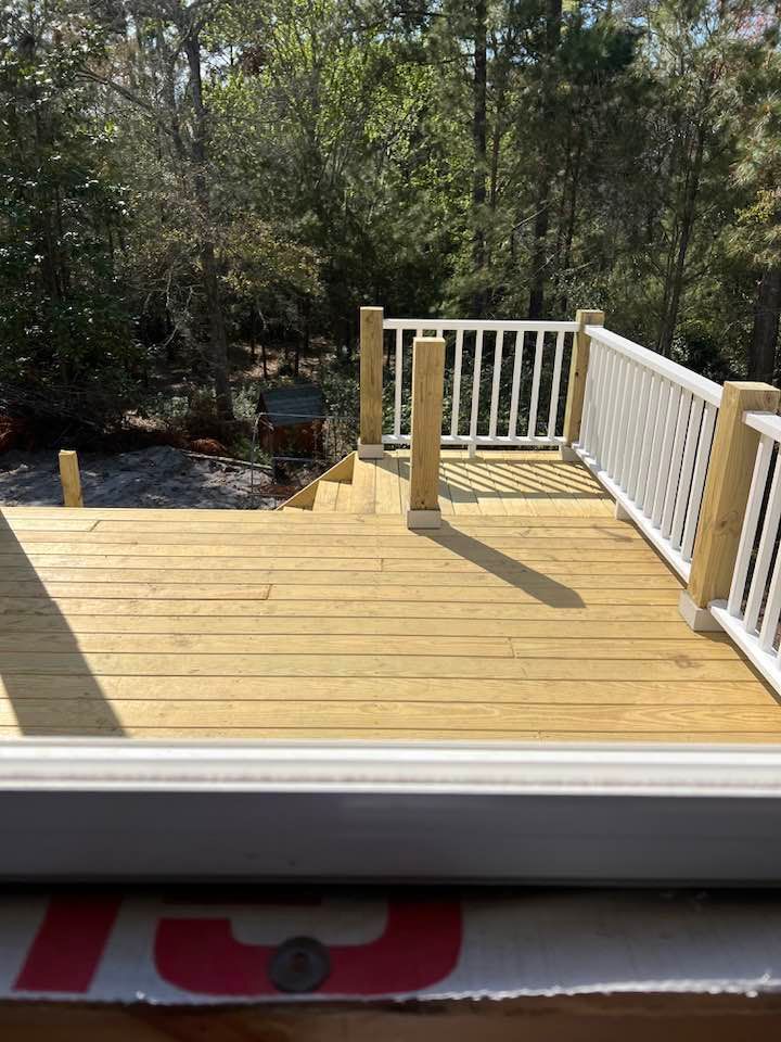 Wooden deck with white railings, steps, and surrounding trees.