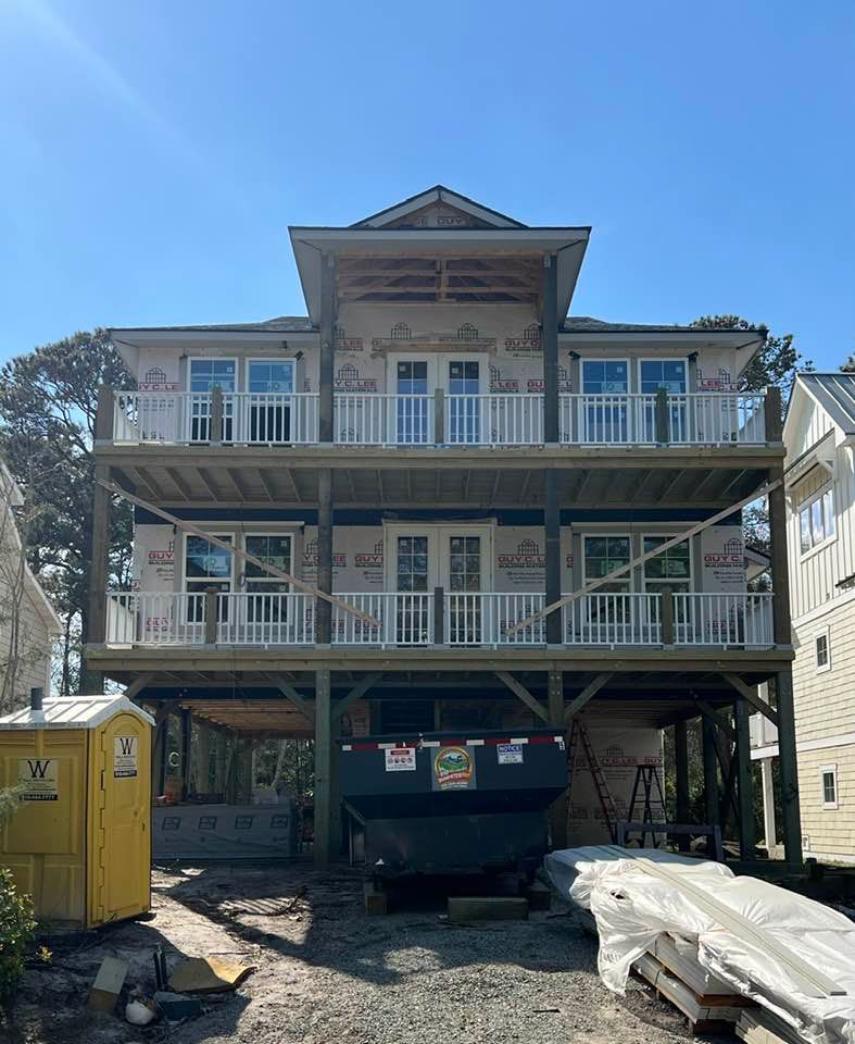 A multi-story house under construction with balconies, a dumpster, and a portable toilet.