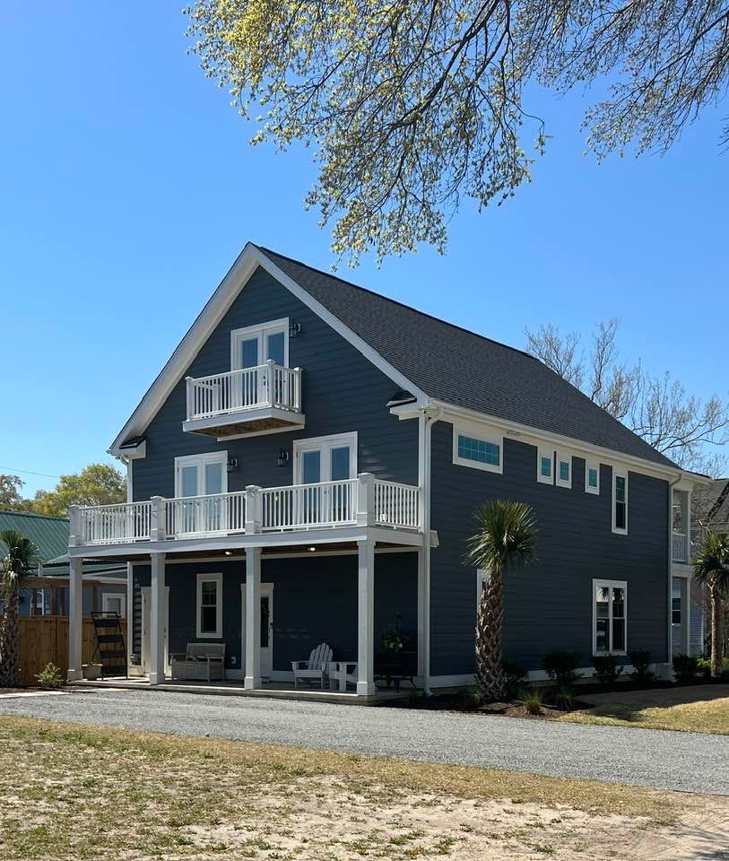 Two-story blue house with white trim, balconies, and a palm tree under a blue sky.