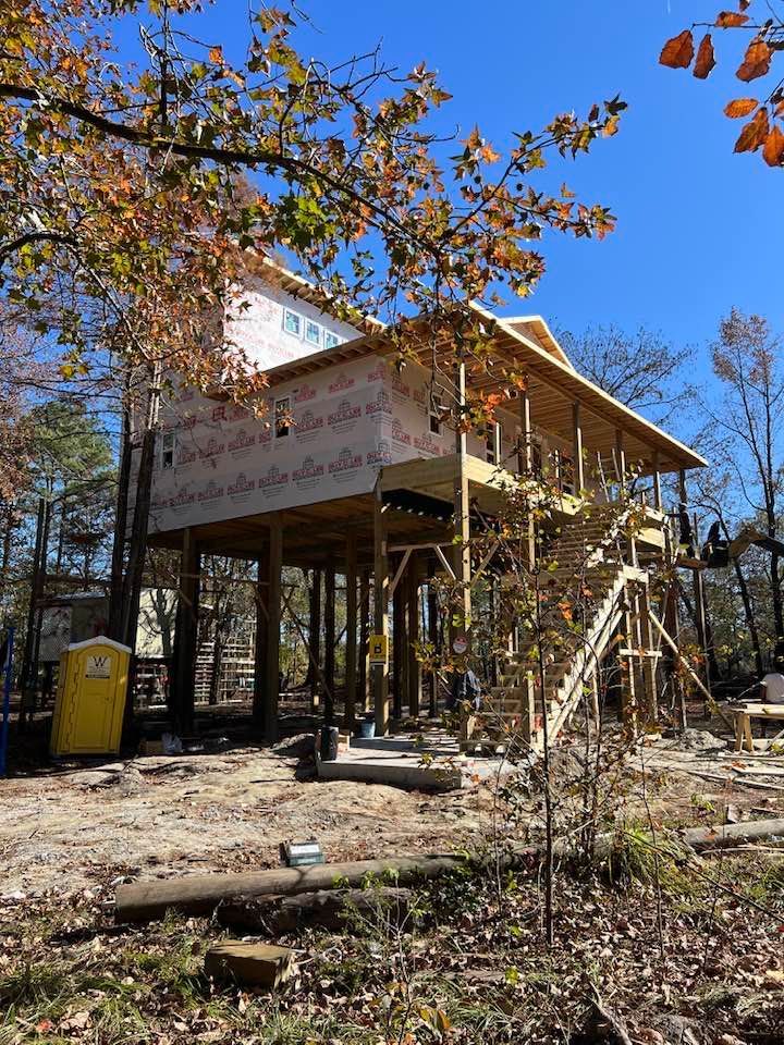 Yellow construction forklift in front of a partially built wooden structure surrounded by trees.