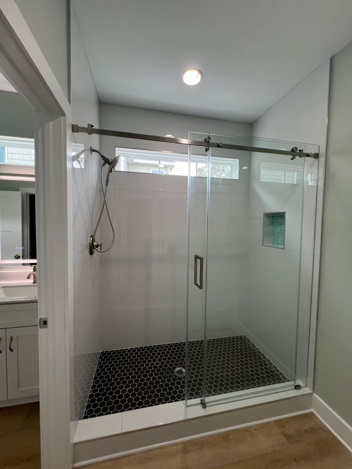 Modern bathroom with a glass-enclosed shower, featuring black tiled floor and white tiled walls.