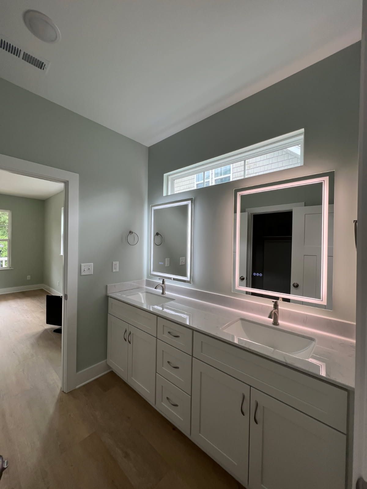 Bathroom with double vanity, light-up mirrors, white cabinets, and light blue walls.