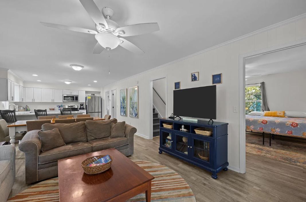 Open-concept living space with sofa, TV, and kitchen. Blue accents, neutral walls, and a view into a bedroom.