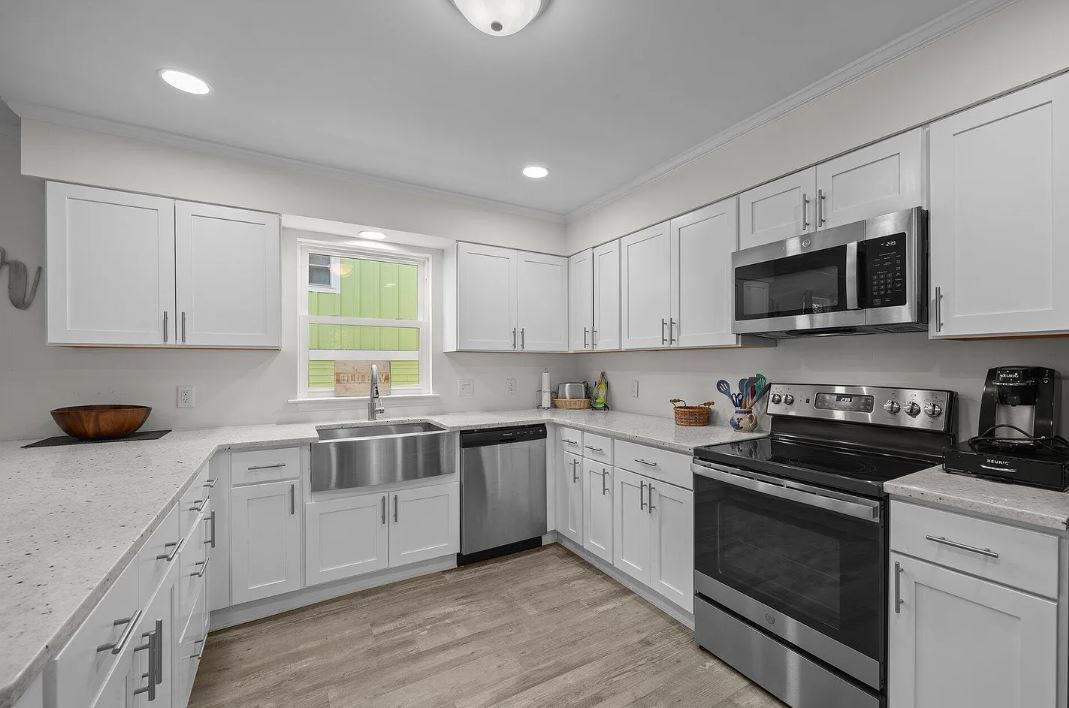 White kitchen with stainless steel appliances and light wood floors.