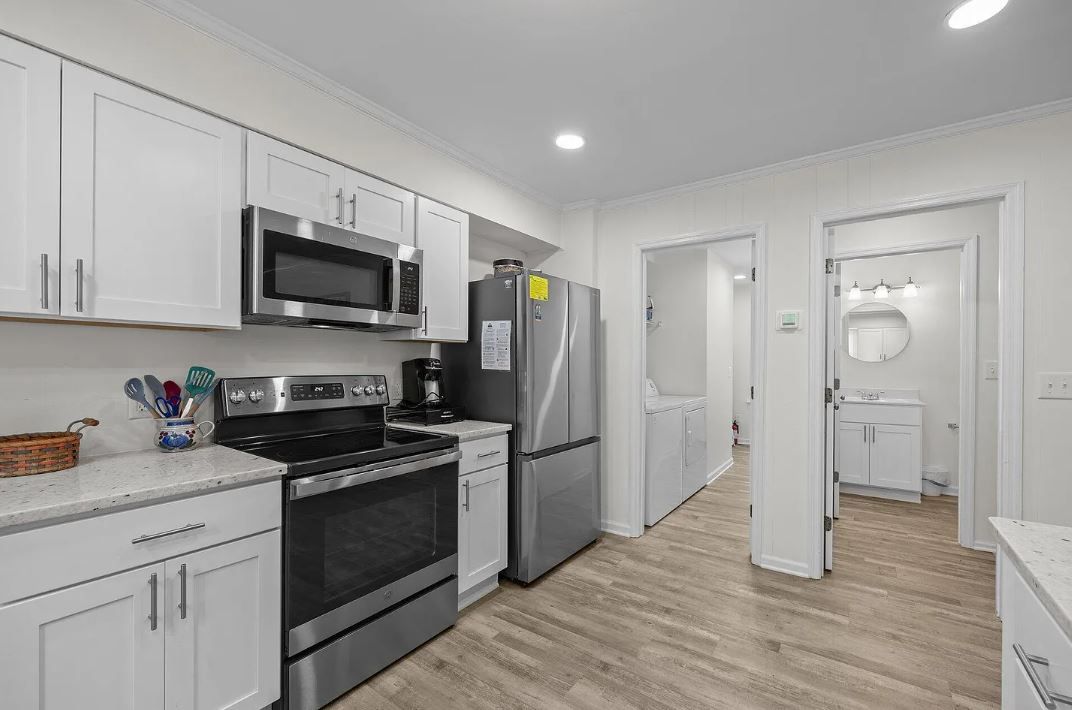 White kitchen with stainless steel appliances and doorway to laundry and bathroom.