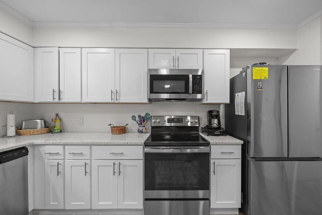 White kitchen with stainless steel appliances, white cabinets, and light countertops.