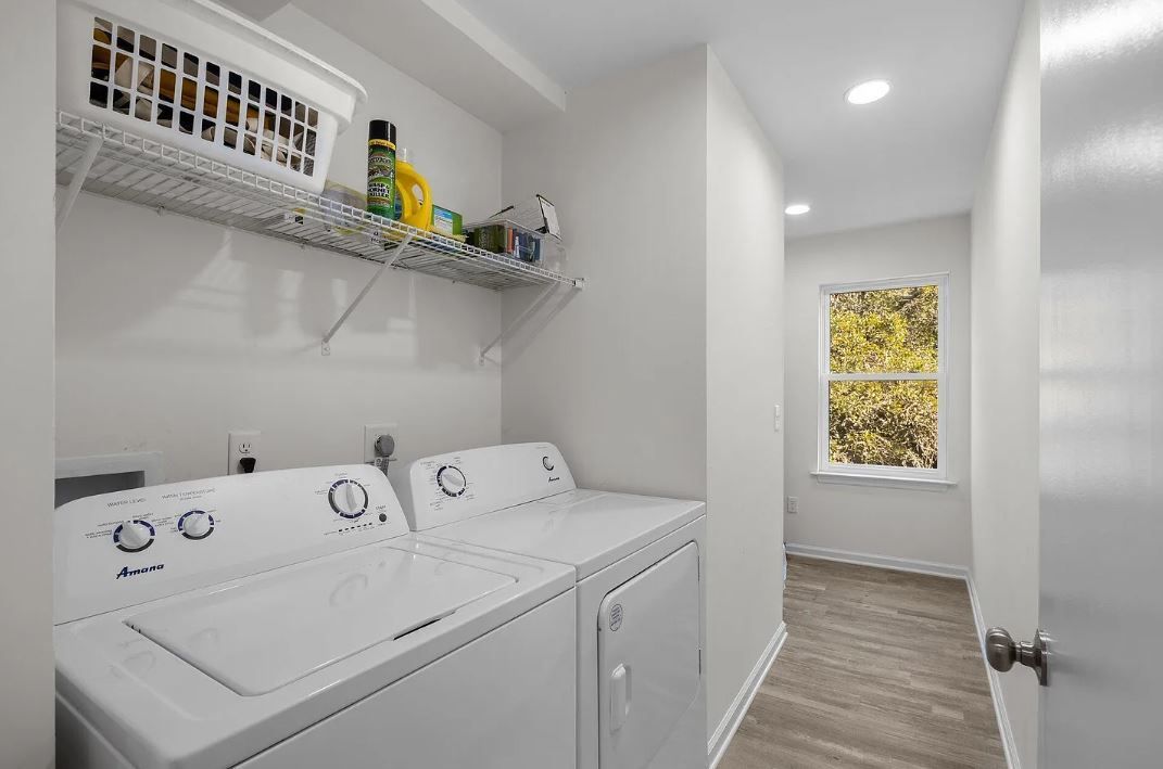 Laundry room with washer, dryer, wire shelf holding cleaning supplies. Hallway with window visible.