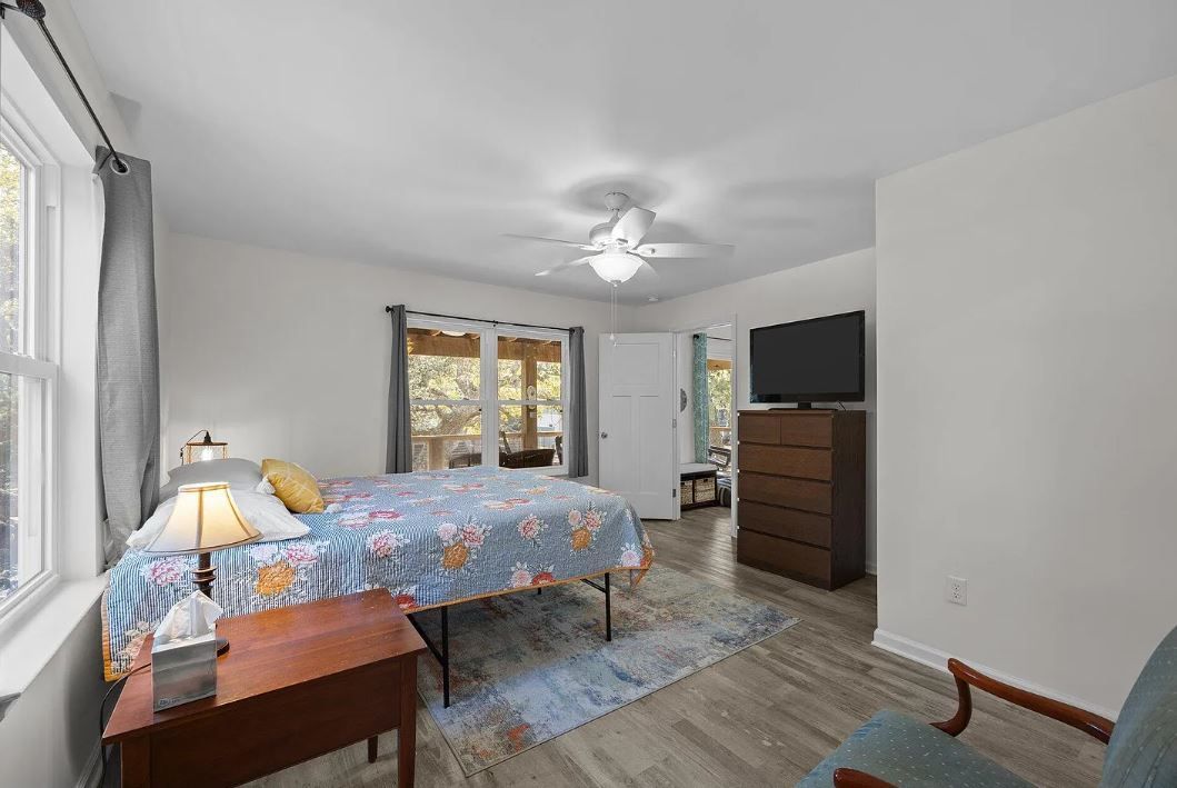 Bedroom with a bed, dresser, table, window, and doors leading to a deck.