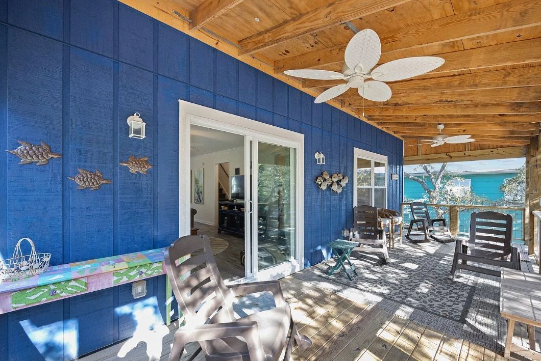 Blue-walled porch with sliding glass door, patio furniture, ceiling fans, and a view of blue water.