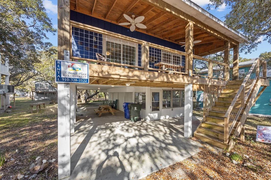 Elevated wooden house with shaded ground-level parking, blue accents, and open-air deck.