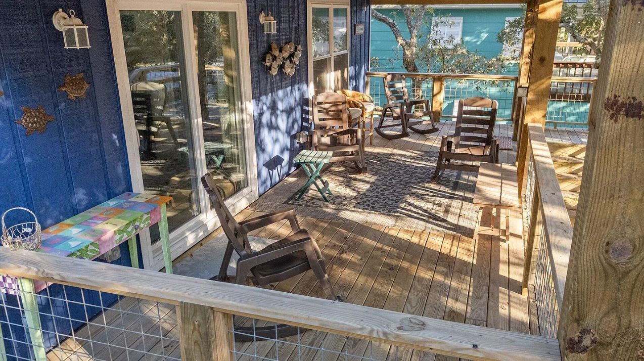 Blue wooden deck with seating, doors to the house, and view of water.