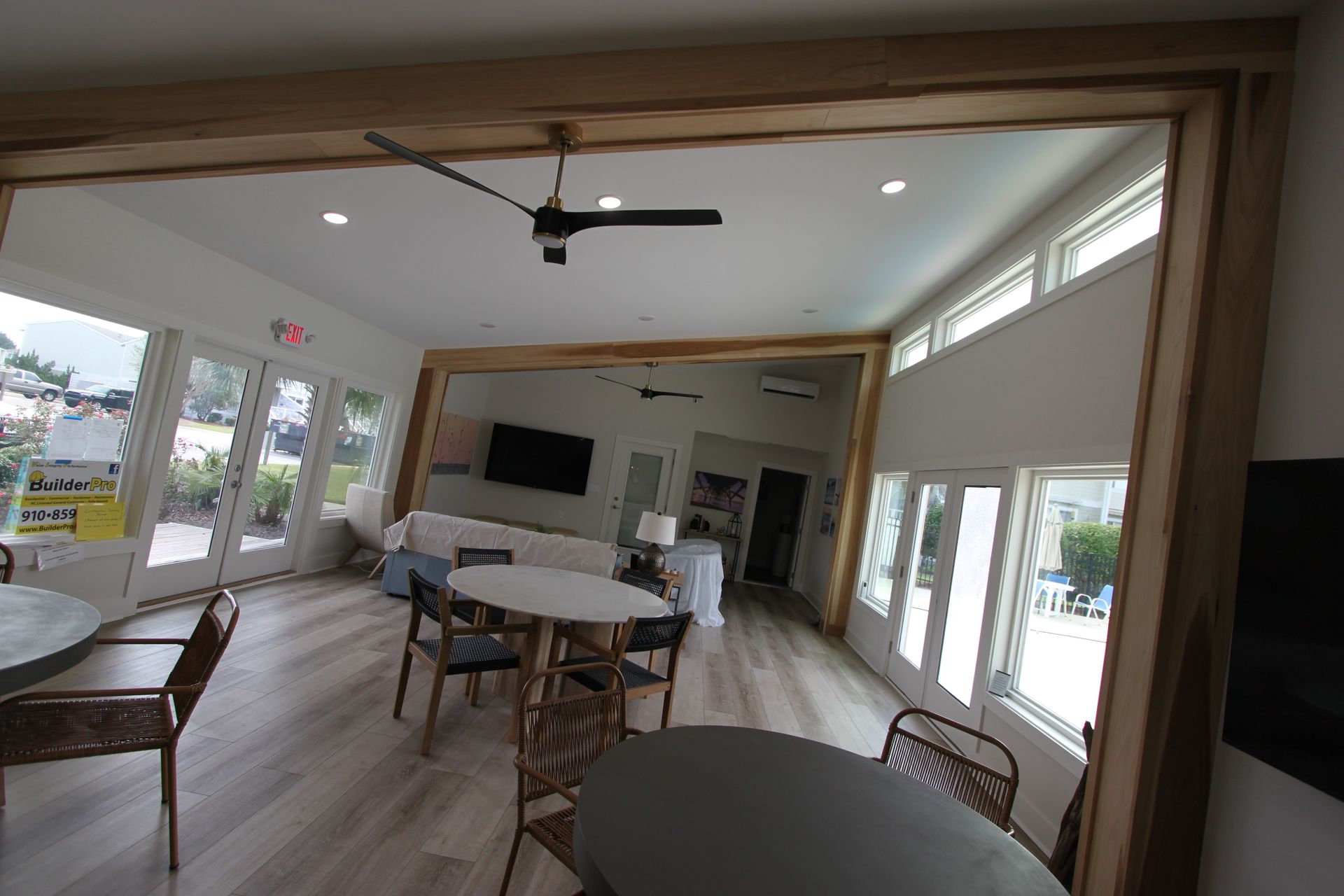 A light-filled room with tables, chairs, and a window reflecting a seating area with a television.