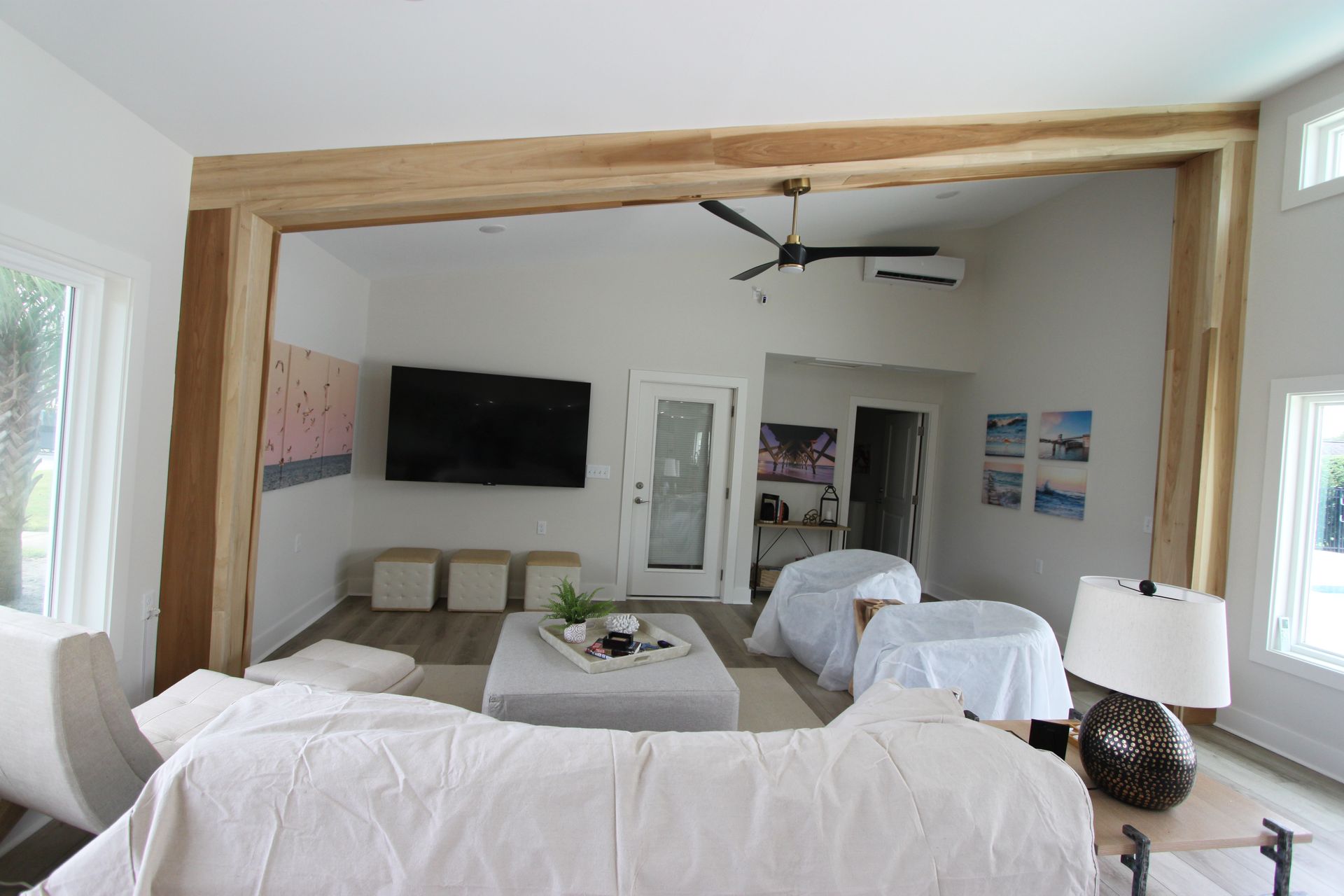 Living room with wooden beams, television, white walls, and covered furniture.