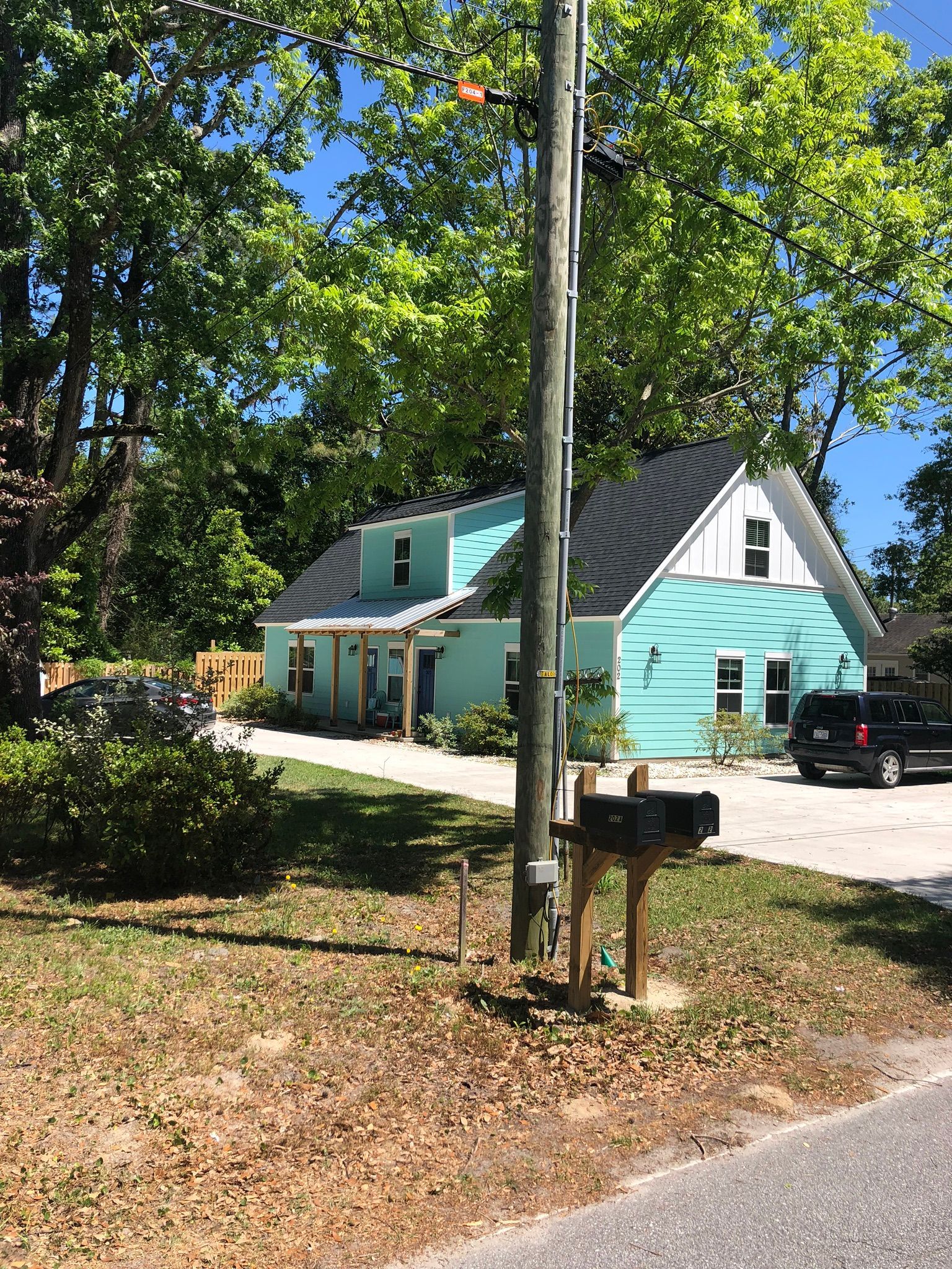 Teal house with black roof, driveway, and mailbox in front; trees surround.