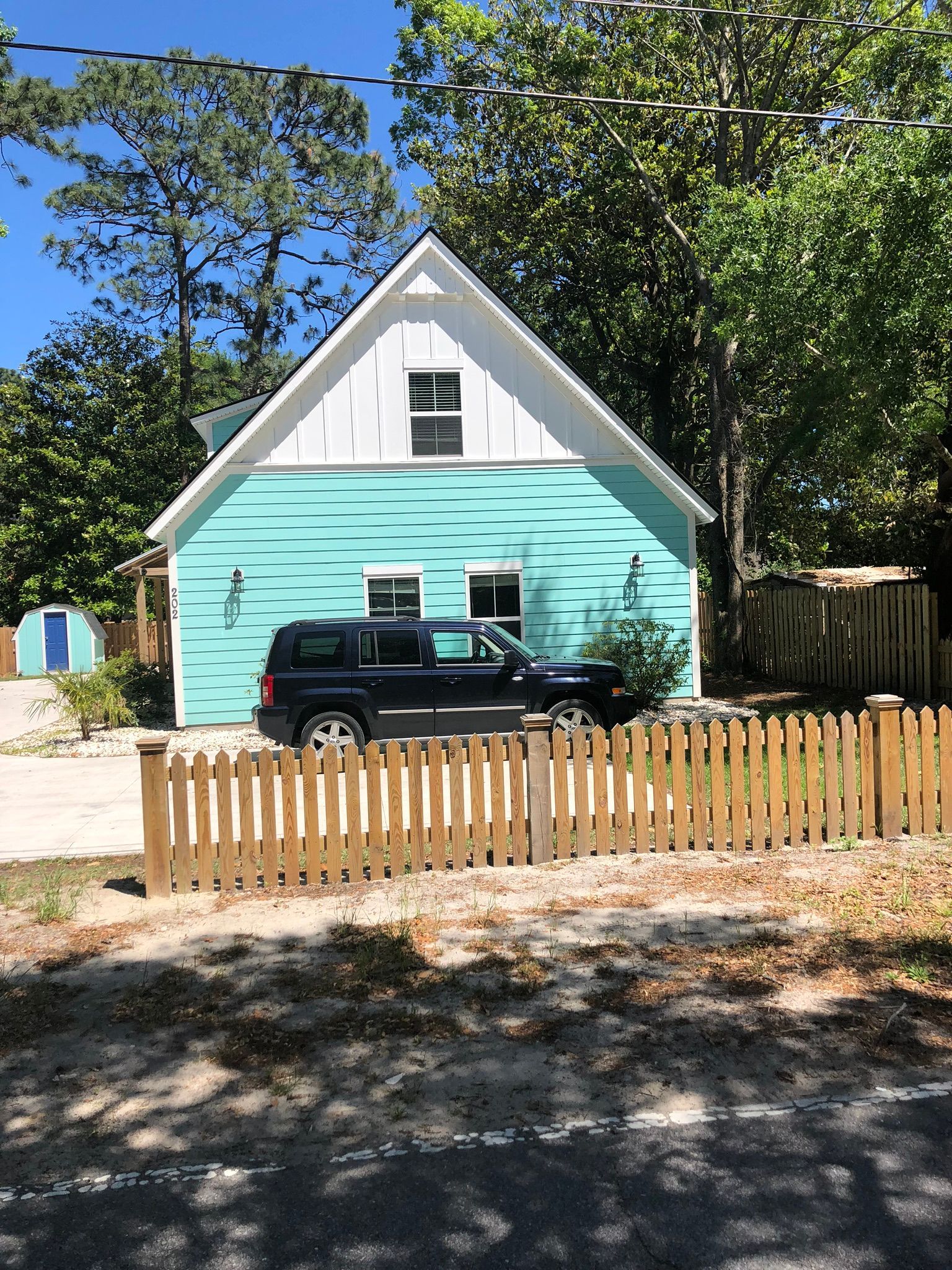 Teal house with white trim, a black SUV, and a wooden picket fence.