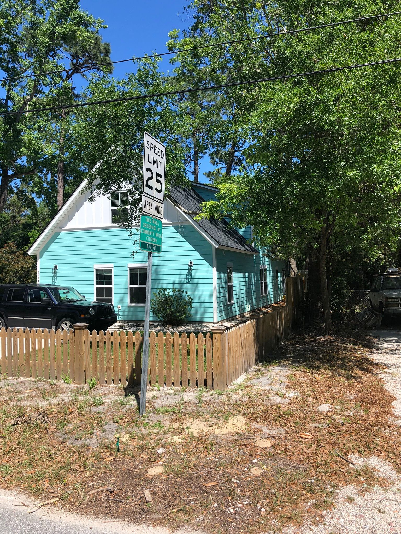 Teal house with a wooden fence and a speed limit sign, surrounded by trees and a car.