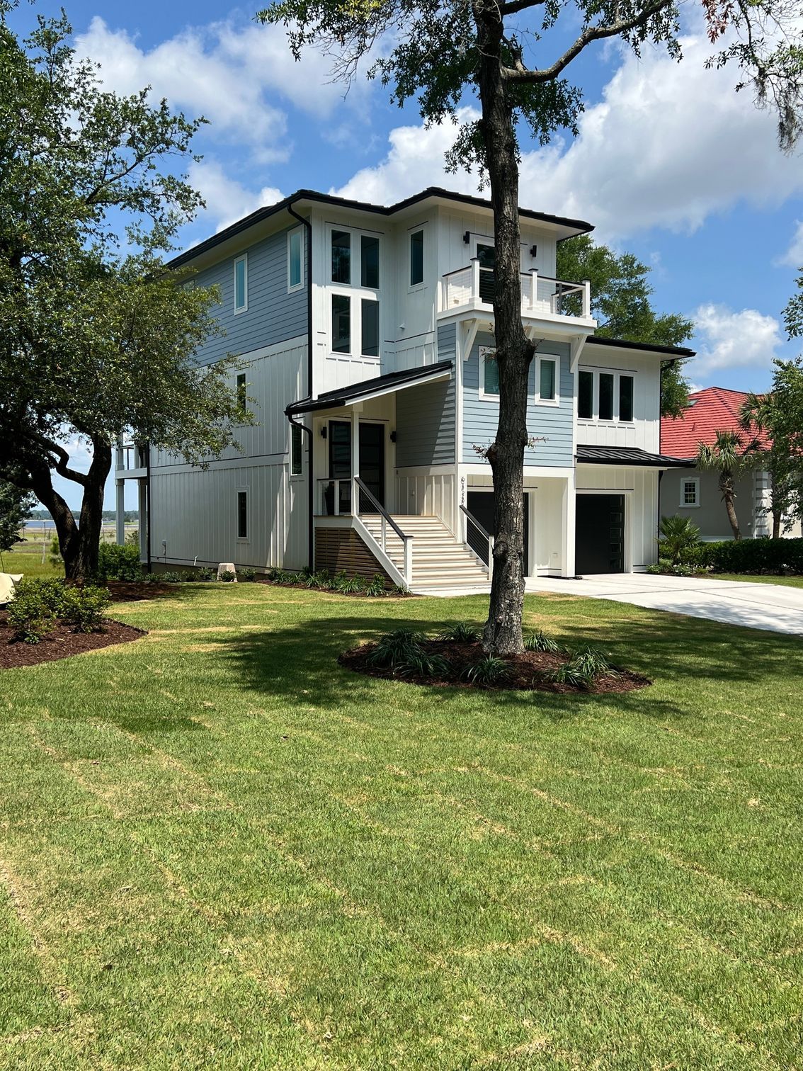 Modern two-story house with blue siding, white trim, and a black roof. Green lawn in front.