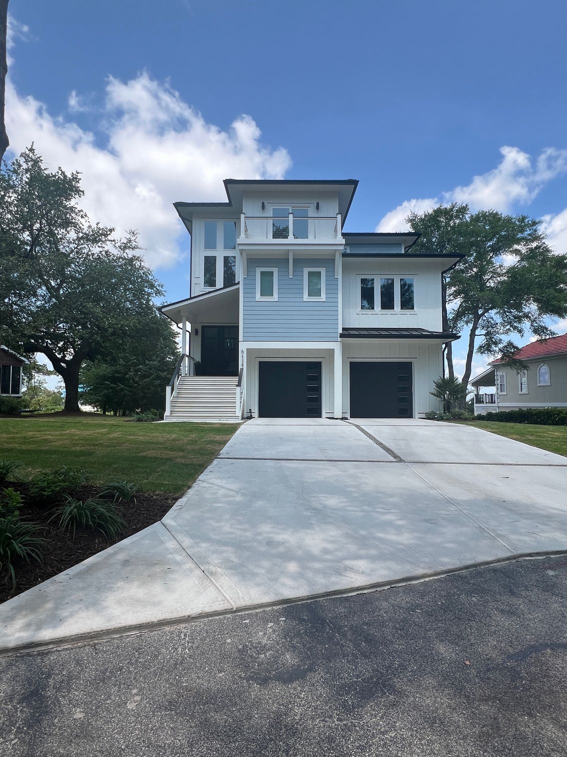Modern two-story house with gray garage doors, light blue siding, and a concrete driveway on a sunny day.