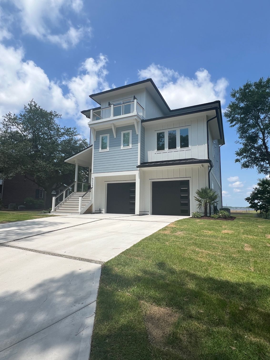 Two-story house with light blue siding, white trim, and black garage doors, driveway, and green lawn.