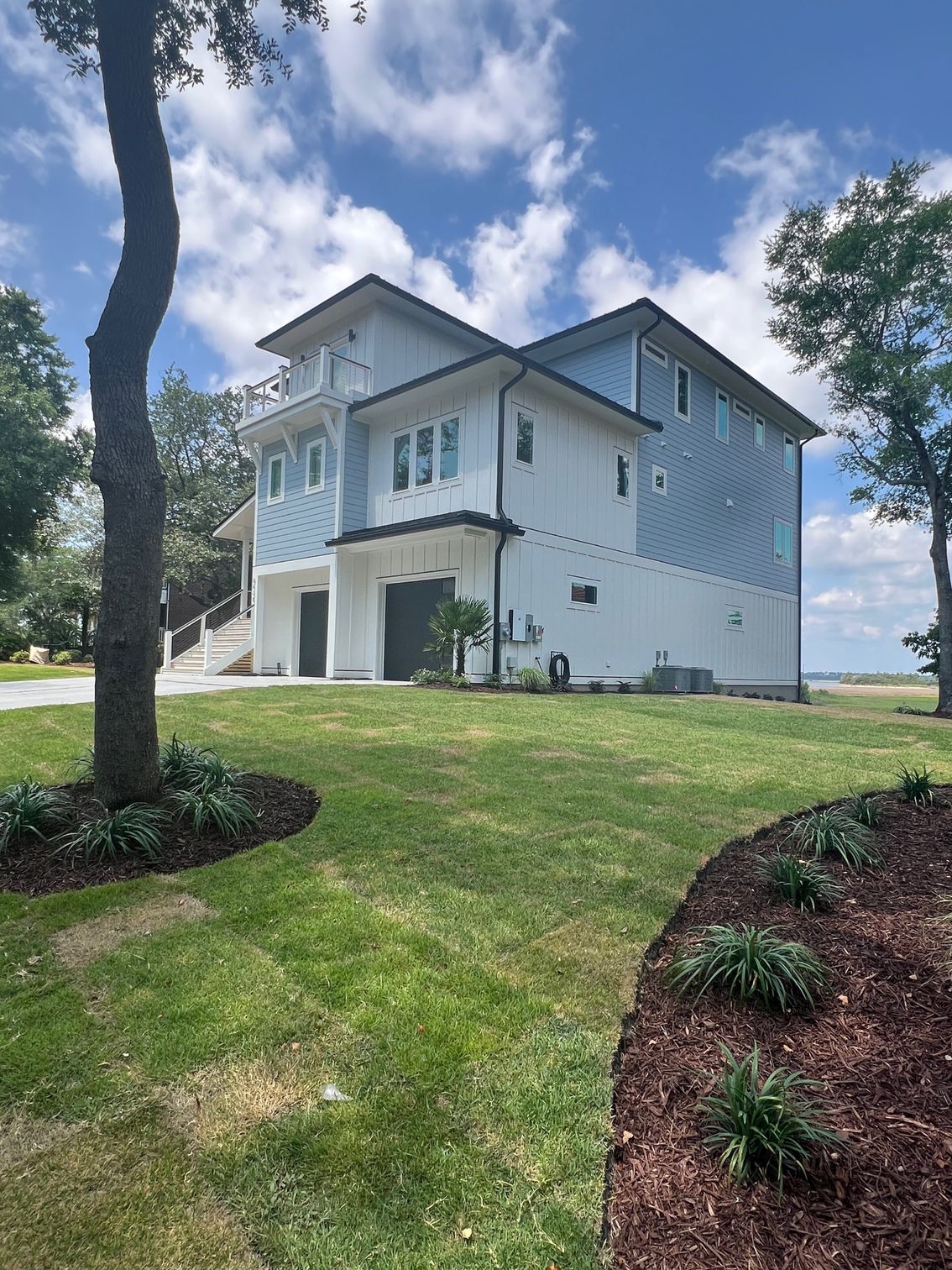 Coastal house with white and blue siding, green lawn, and blue sky with clouds.