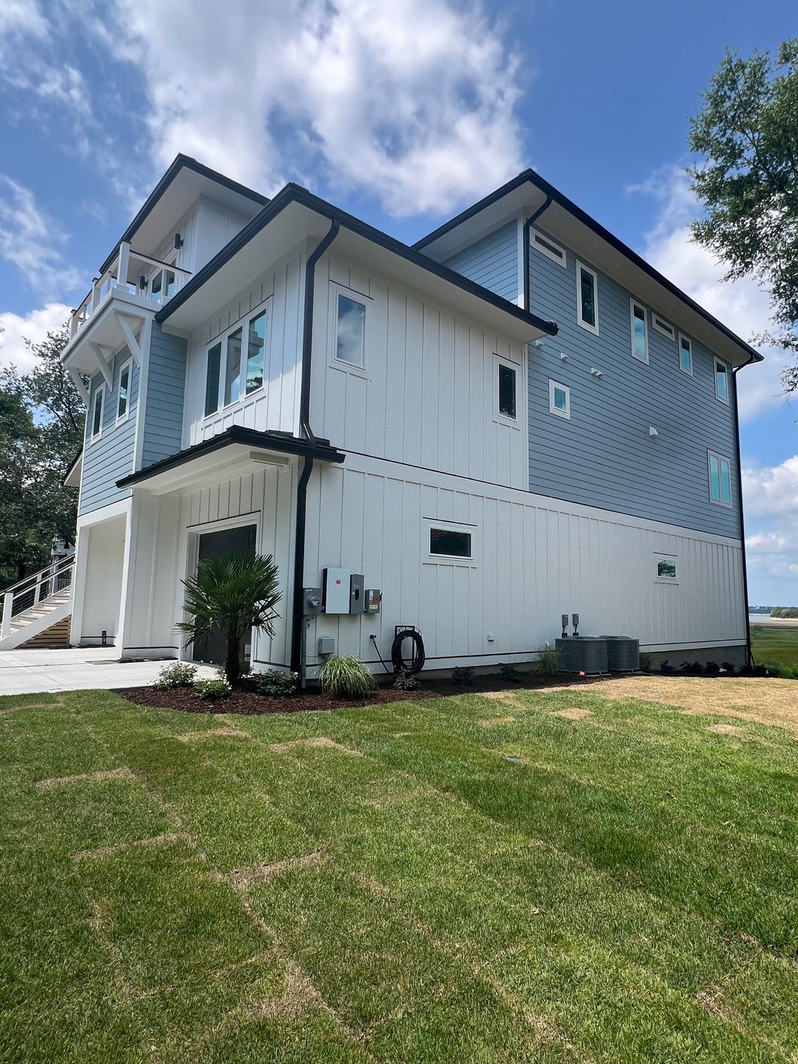 Modern two-story house with blue and white siding, black trim, and green lawn against a cloudy sky.