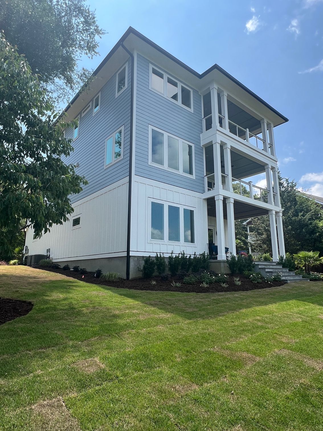 Three-story house with blue siding, white trim, and multiple balconies, set on a green lawn.
