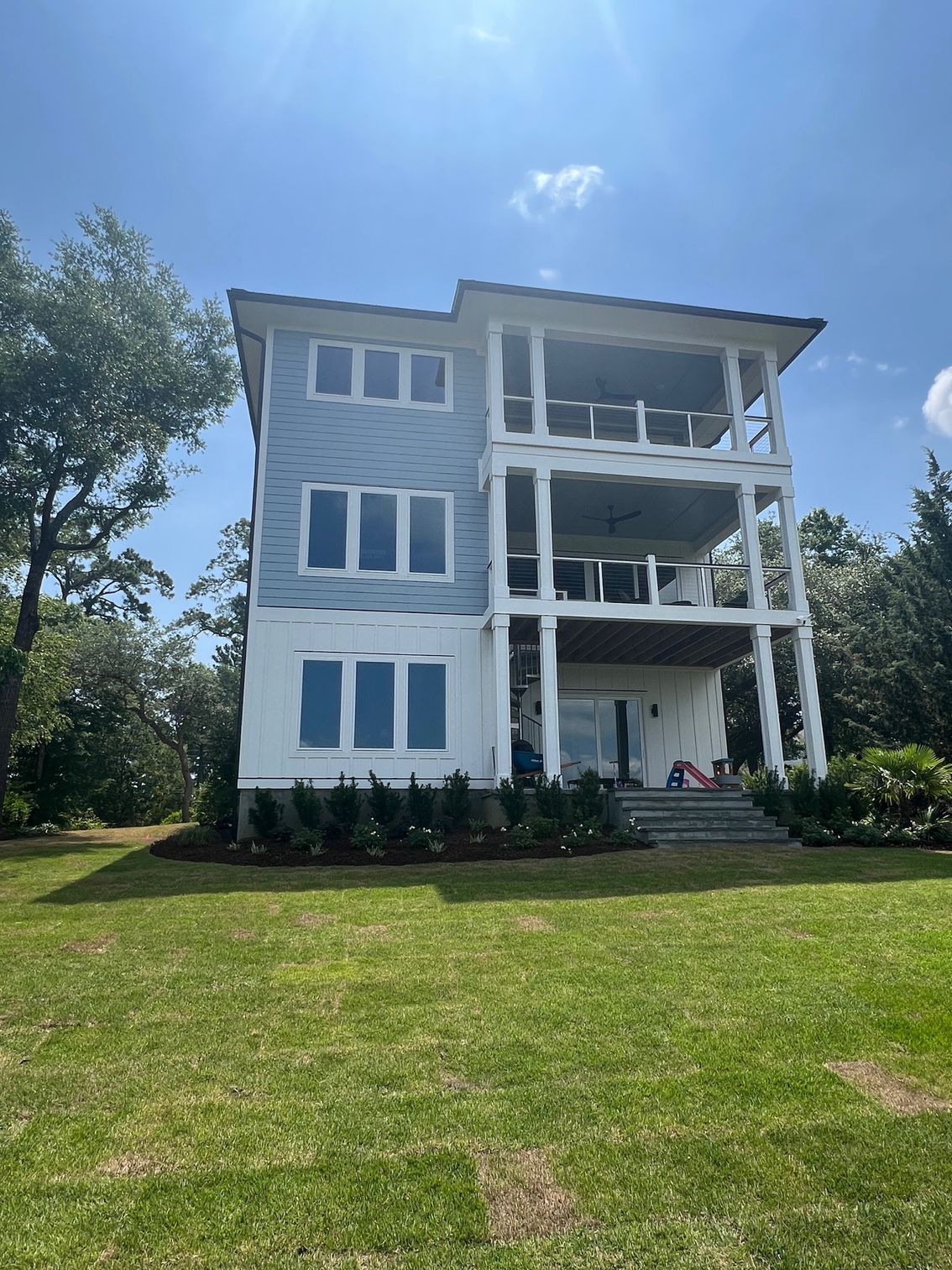 Three-story house with light blue siding and multiple balconies, on green grass.