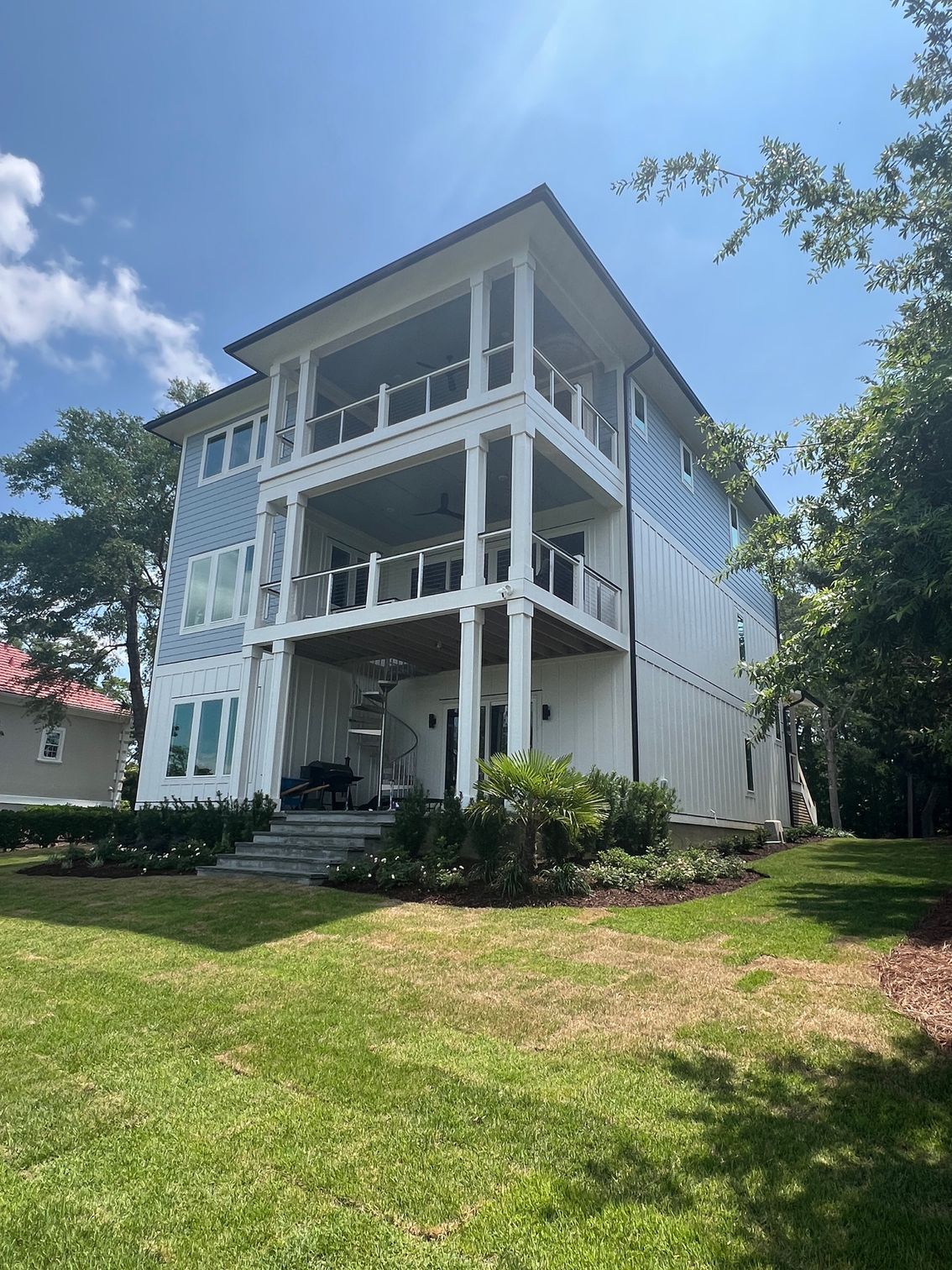 Multi-story blue and white house with balconies, glass railings, and landscaping under a sunny sky.