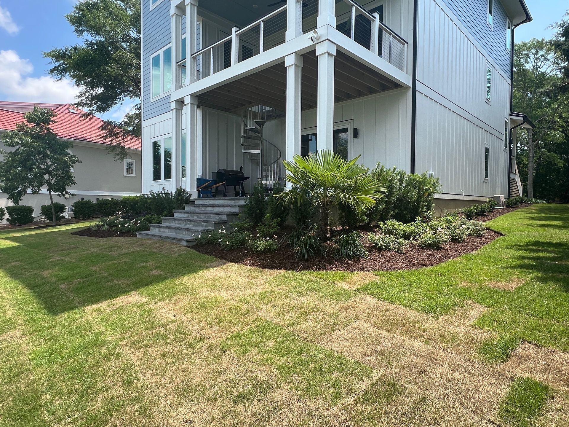 Two-story white house with blue accents and a green lawn. Landscaping with bushes and flowers. Sunny day.