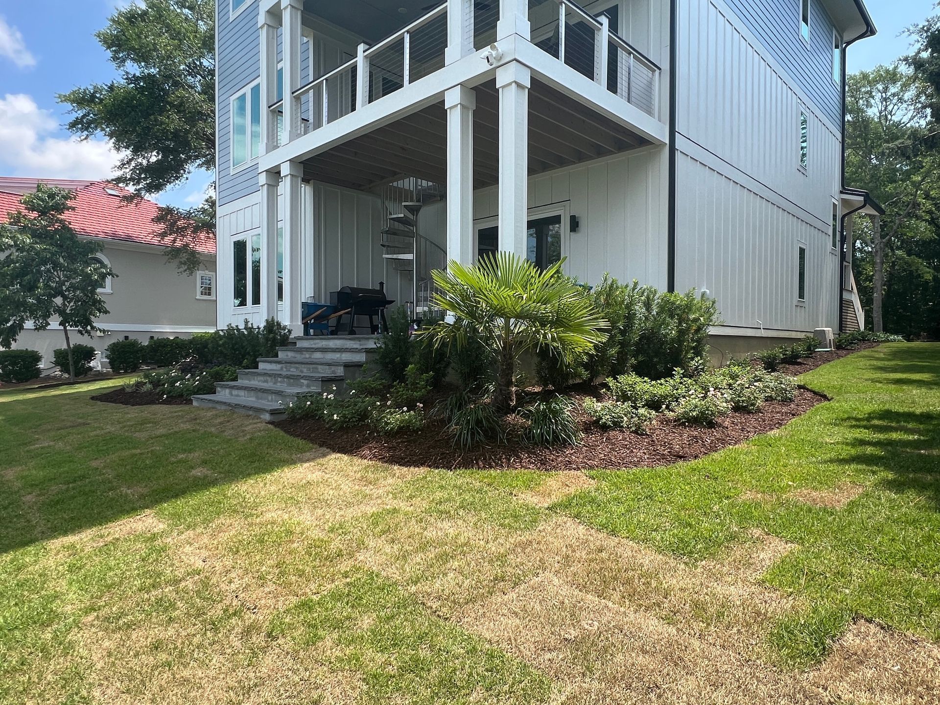 Two-story house with white siding and a balcony, surrounded by green grass and landscaping.