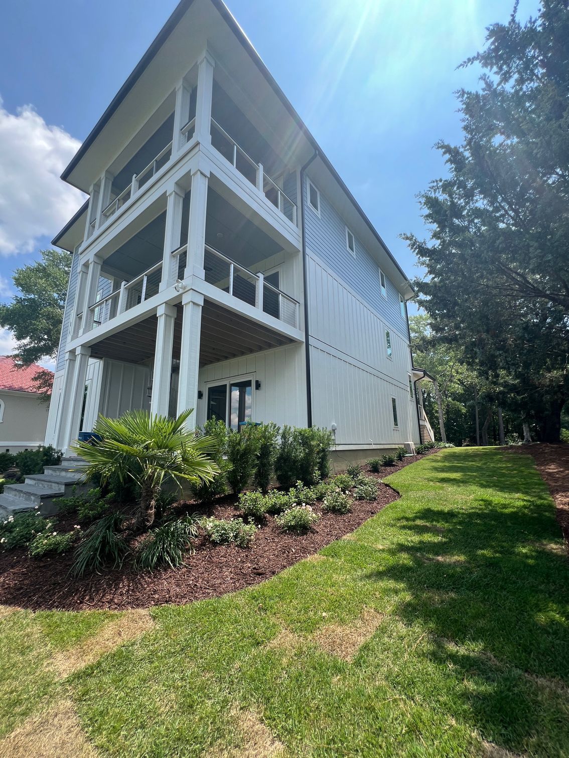 White multi-story house with balconies, landscaping, and blue sky.