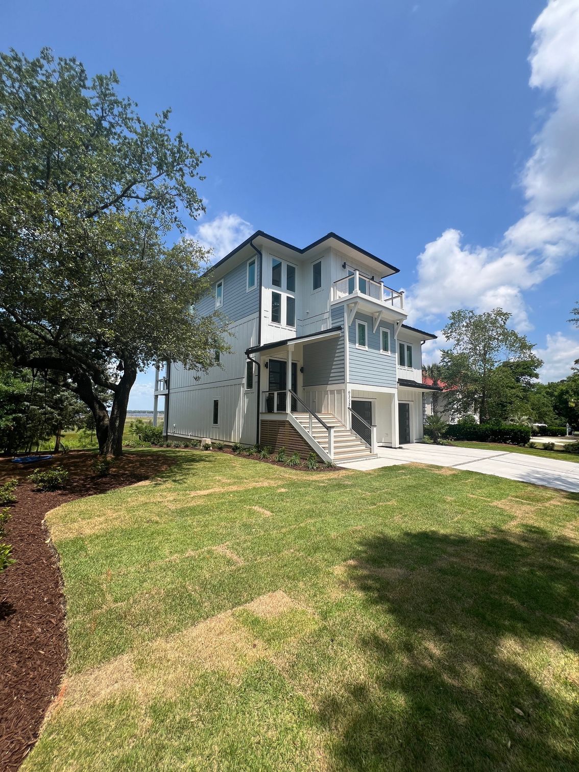 Two-story house with blue siding, white trim, and a porch, on a green lawn under a blue sky.