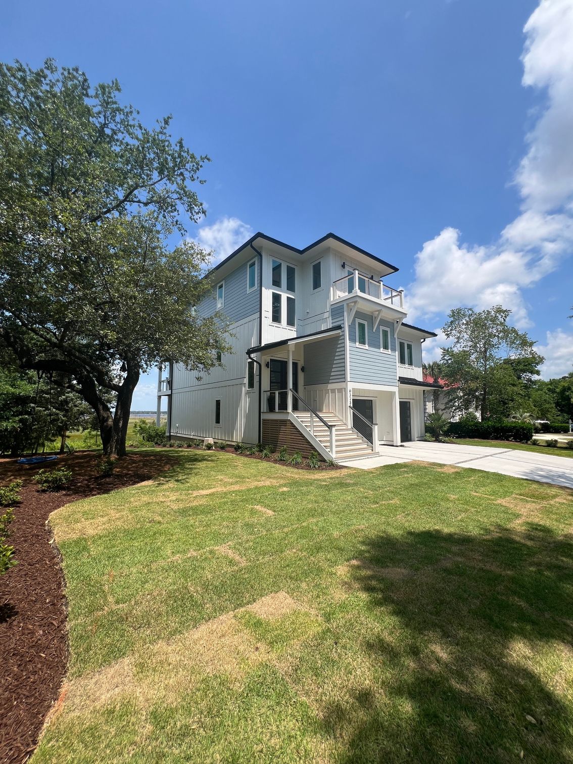 Three-story modern home with blue siding, white trim, and a green lawn under a partly cloudy sky.