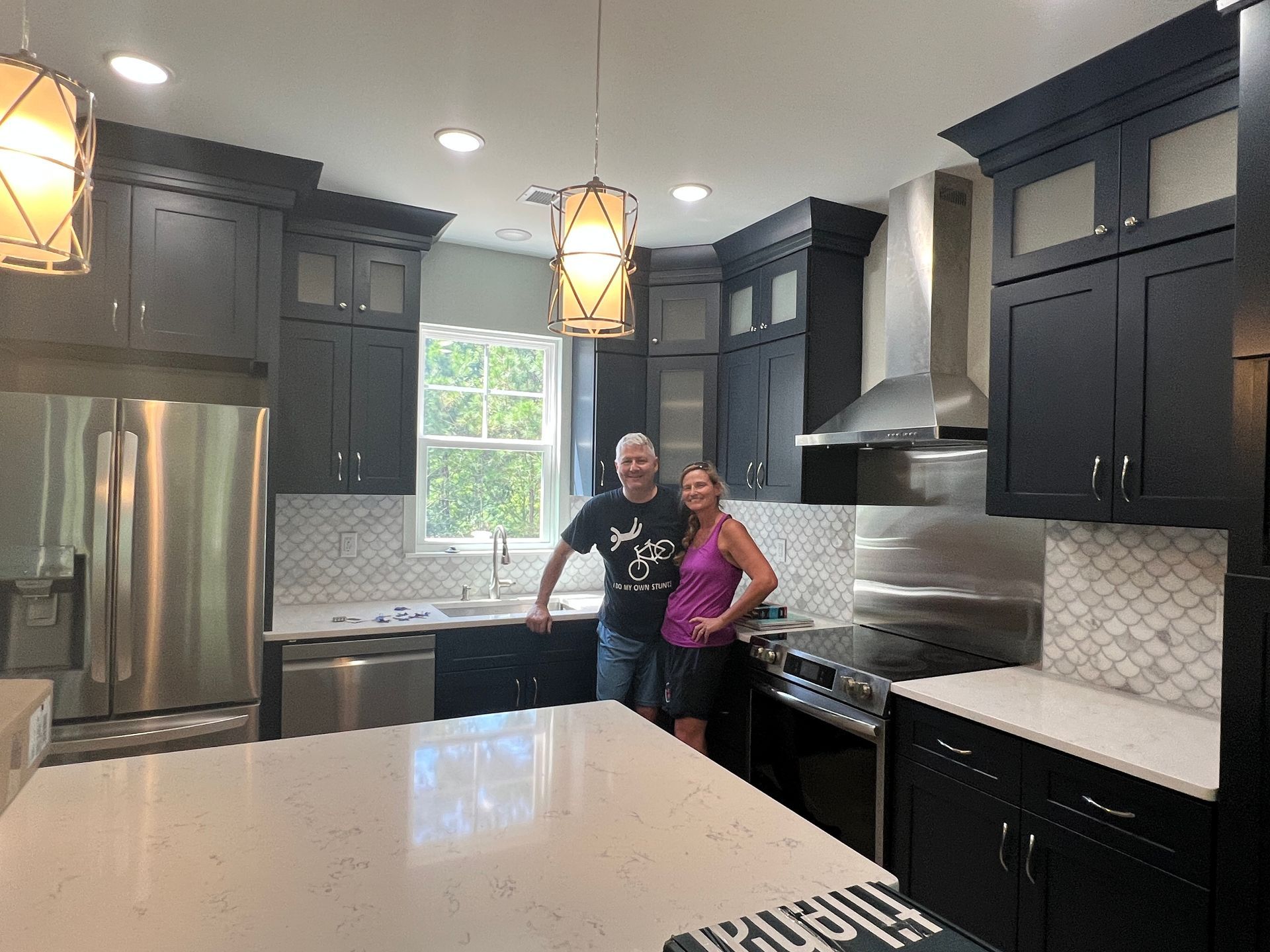 Couple standing in a remodeled kitchen with dark cabinets, stainless steel appliances, and a white countertop.