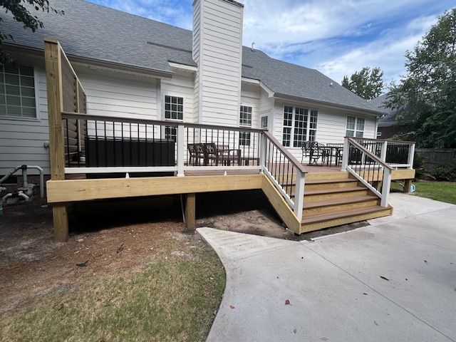 Backyard deck with dark railing and stairs, attached to a white house with a chimney.