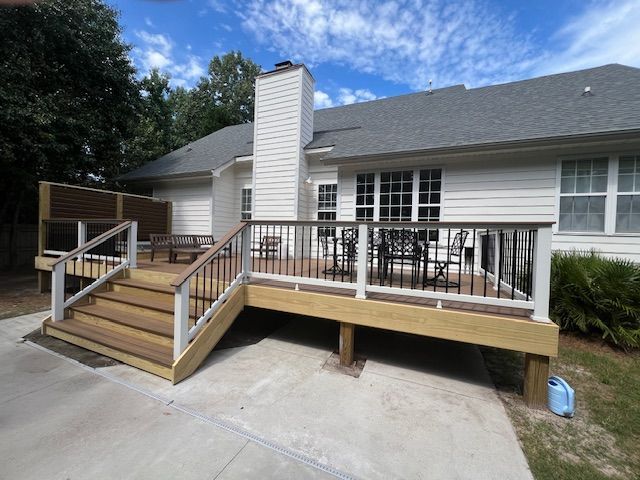 Backyard deck with steps, railings, and seating. House in background, blue sky.