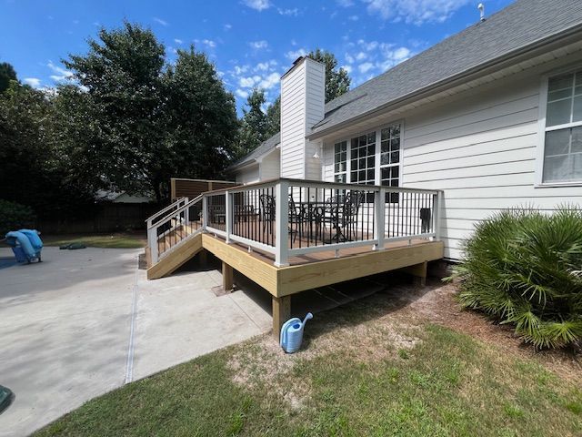 A newly built wooden deck with white railing, and a small black wrought iron table and chairs
