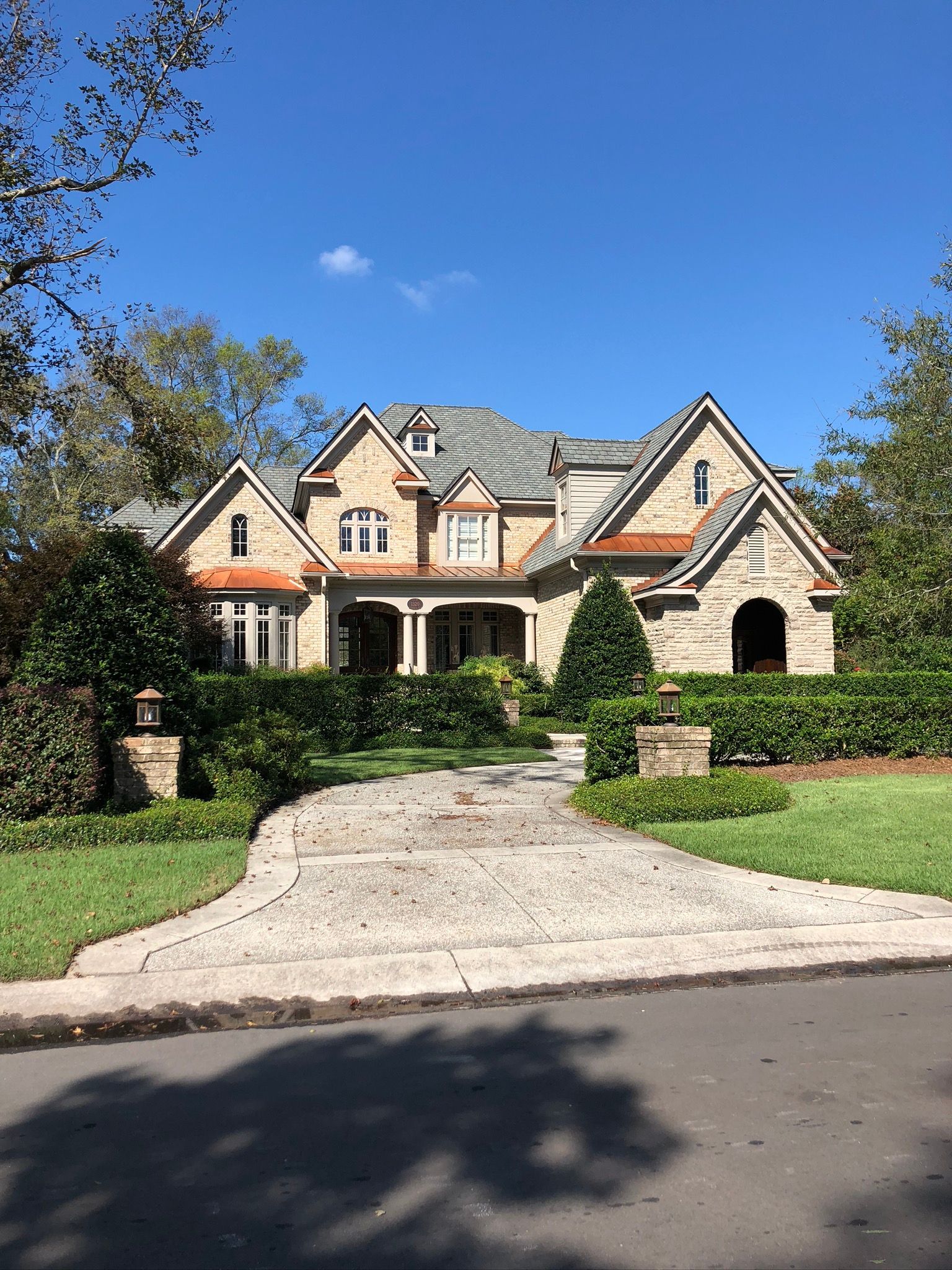 Stone-clad house with a gray roof and copper accents. Green landscaping, and blue sky.