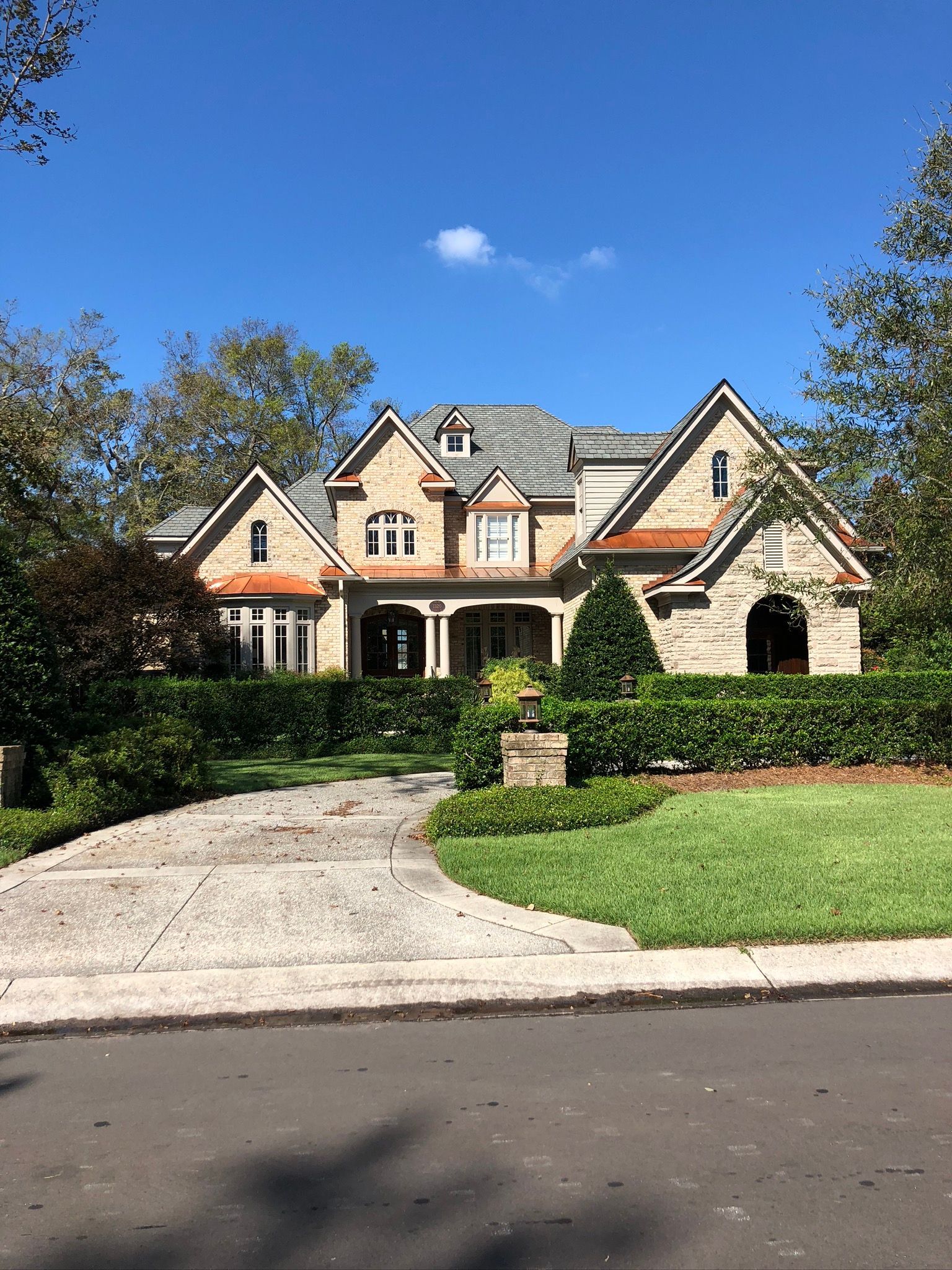 Stone house with gabled roof, driveway, and manicured landscaping under a blue sky.