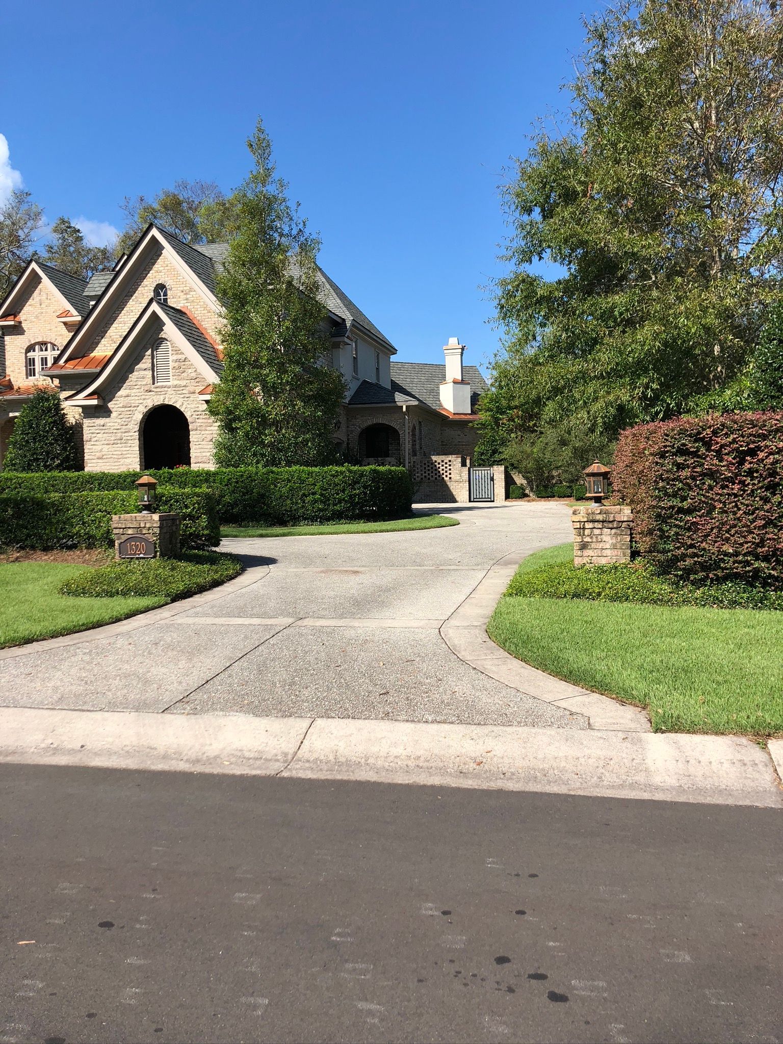 Stone house with a winding driveway, lush landscaping, and clear blue sky.