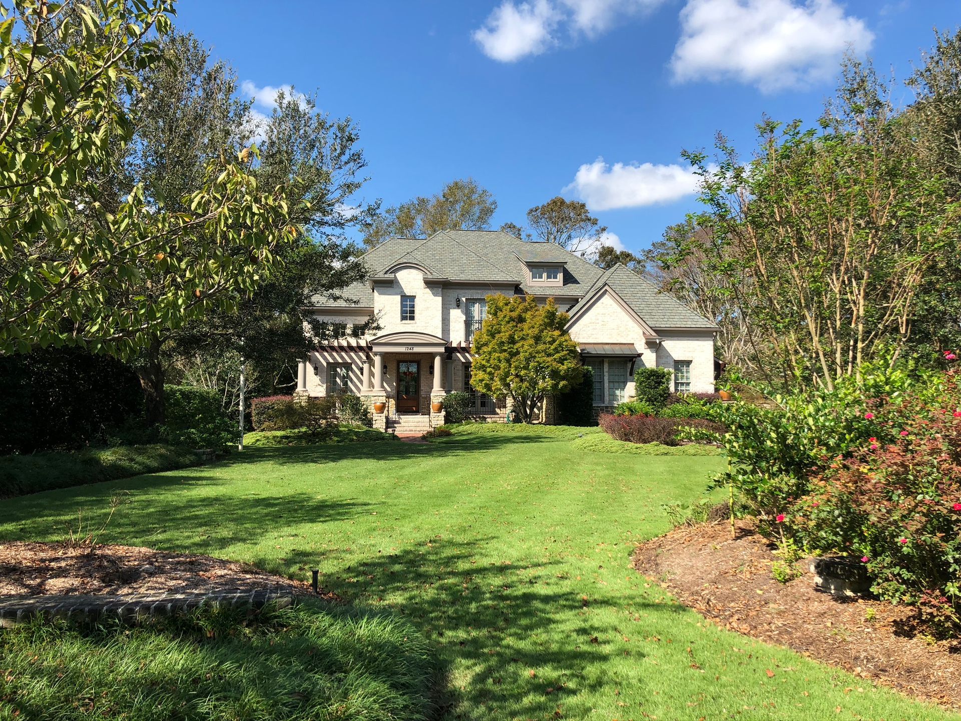Two-story house with green lawn, trees, and blue sky.