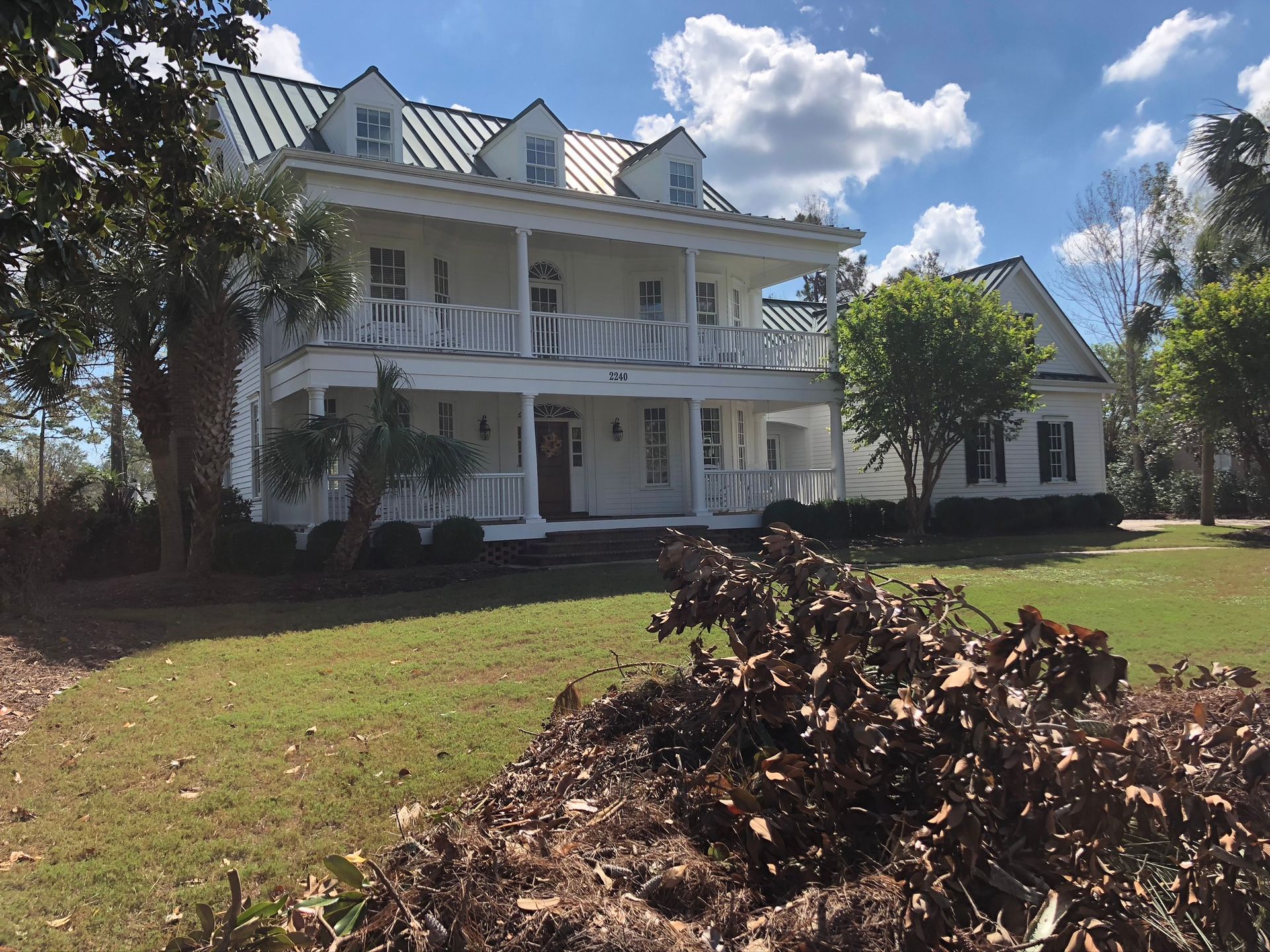 White two-story house with green metal roof, front porch, and dormers on a sunny day.