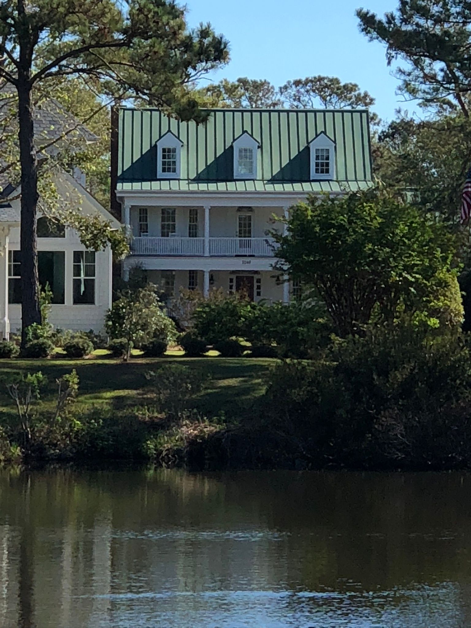 Two-story white house with green metal roof and three dormers, overlooking water.